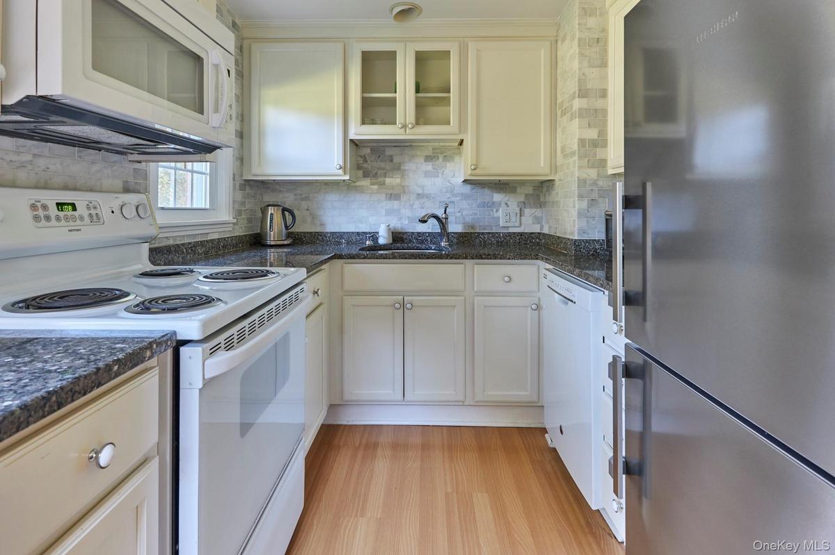 Kitchen featuring white appliances, glass insert cabinets, backsplash, light wood-style flooring, and white cabinetry