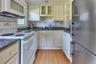 Kitchen featuring white appliances, glass insert cabinets, backsplash, light wood-style flooring, and white cabinetry