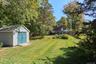 View of green lawn with a storage unit and view of wooded area