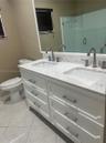 Dual-sink vanity with white cabinetry, light-toned stone-finish countertop, undermount rectangular sinks, brushed nickel hardware, and large wall-to-w
