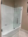 Bathtub featuring white tile surround, frameless glass door with brushed metal hardware, and integrated soap dish