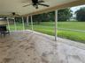 Screened-in patio featuring tile flooring, dual ceiling fans, and an exterior rock border overlooking a grass lawn with mature trees