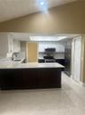 Kitchen featuring high-contrast white and dark cabinetry, quartz countertops, stainless steel appliances, a vaulted ceiling, and tile flooring