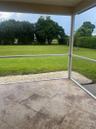 Screened-in patio with large-format tile flooring, perimeter stone landscaping, and an expansive lawn