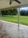 Screened-in patio featuring tile flooring, a ceiling fan, and access to a landscaped backyard with mature trees