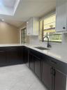 Kitchen featuring high-contrast cabinetry, stone countertops, stainless steel sink with matte black gooseneck faucet, tile flooring, and a glass-paned