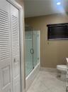Full bathroom featuring a frameless glass shower enclosure, louvered closet doors, tiled flooring, and window blinds