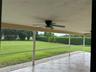 Screened-in patio featuring tile flooring, a ceiling fan, and access to a level lawn with established hedging