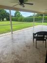 Screened lanai featuring large-format stone-look tile flooring, ceiling fans, and a expansive backyard with a manicured lawn and perimeter hedges