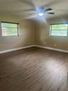 Wood-finish flooring, dual windows with horizontal blinds, and a central ceiling fan with integrated lighting