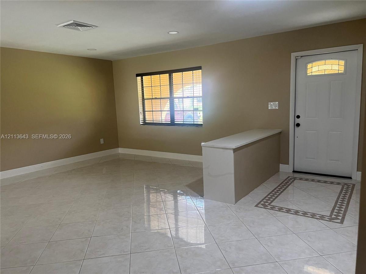 Neutral-toned interior featuring large-format ceramic tile flooring, a built-in counter with a stone-finish top, an exterior door with a decorative tr