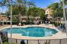 Swimming pool area featuring stone paver decking, a spa, covered pavilion, and metal perimeter fencing surrounded by mature palm trees