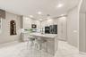 Kitchen featuring flat-panel cabinetry, quartz countertops, a central island with an integrated sink, built-in double wall ovens, and tile flooring