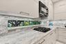 Kitchen featuring high-gloss cabinetry, stone countertops and backsplash, integrated horizontal window, and black gas cooktop with matching built-in m
