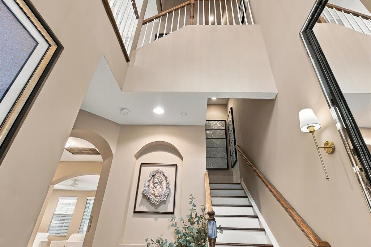 Double-height entry featuring an arched recessed wall niche, staircase with a wood handrail and white balusters, and wall-mounted brass lighting