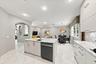 Kitchen featuring light-toned cabinetry, stone-finish countertops, recessed lighting, tile flooring, and a central island with a built-in dishwasher