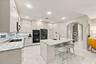 Kitchen featuring light-toned cabinetry, stone countertops, a central island with an integrated sink, built-in double ovens, and recessed lighting