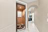 In-home elevator with wood-paneled interior and recessed lighting, featuring an arched entryway and light-toned tile flooring