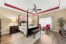 Tray ceiling with recessed architectural detail, wood-finish flooring, and a central ceiling fan with integrated lighting