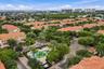 Aerial perspective featuring tile-roofed architecture, palm-lined landscaping, a communal swimming pool, and a coastal horizon
