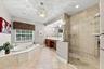 Jetted soaking tub with tile surround, walk-in glass-enclosed shower, dual-sink vanity with built-in cabinetry, crystal-accented light fixture, and ti
