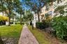 Brick paver walkway lined with mature trees, established landscaping, and black metal fencing