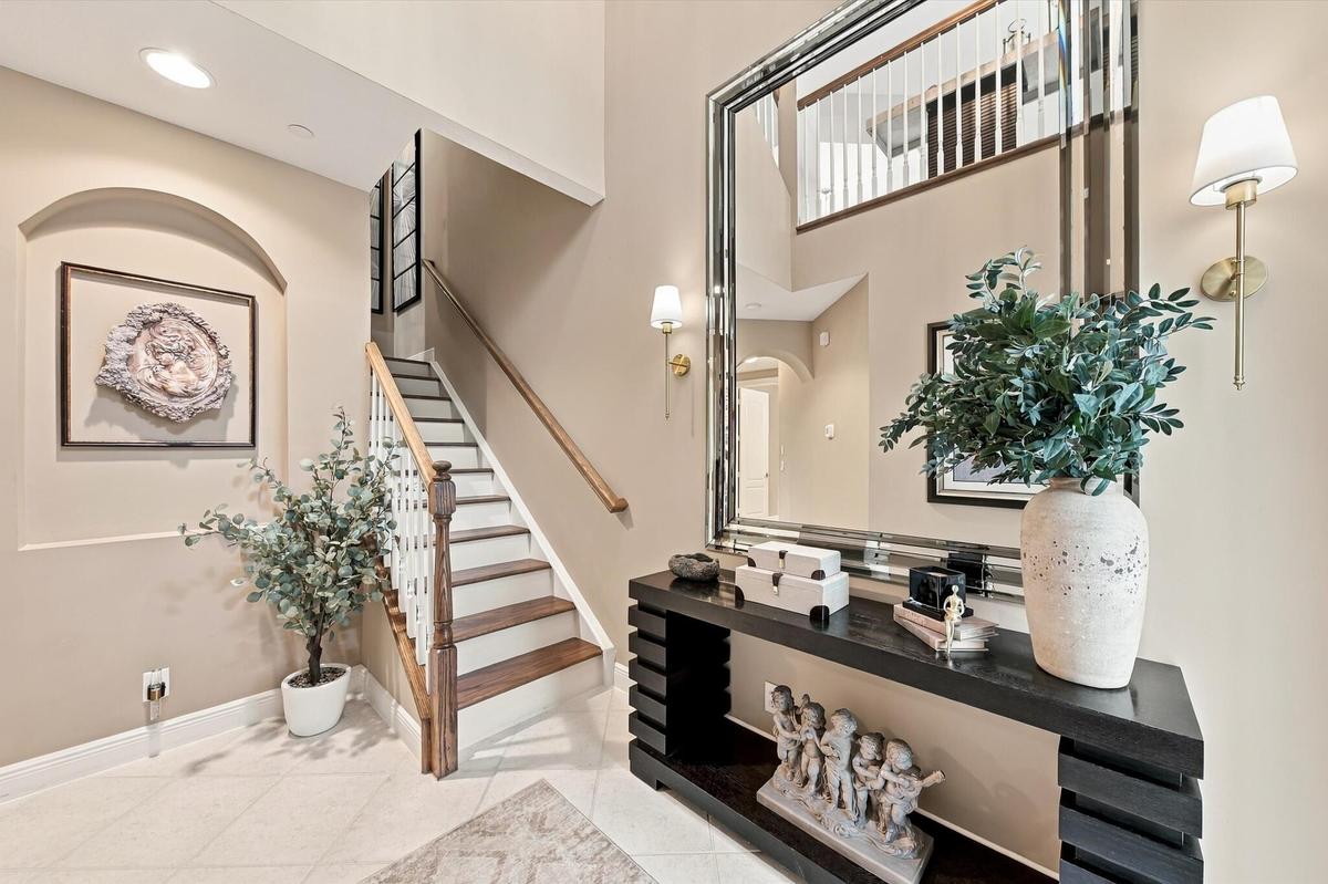 Two-story foyer featuring tile flooring, an arched recessed wall niche, a staircase with wood-finish treads and a white balustrade, and wall-mounted l