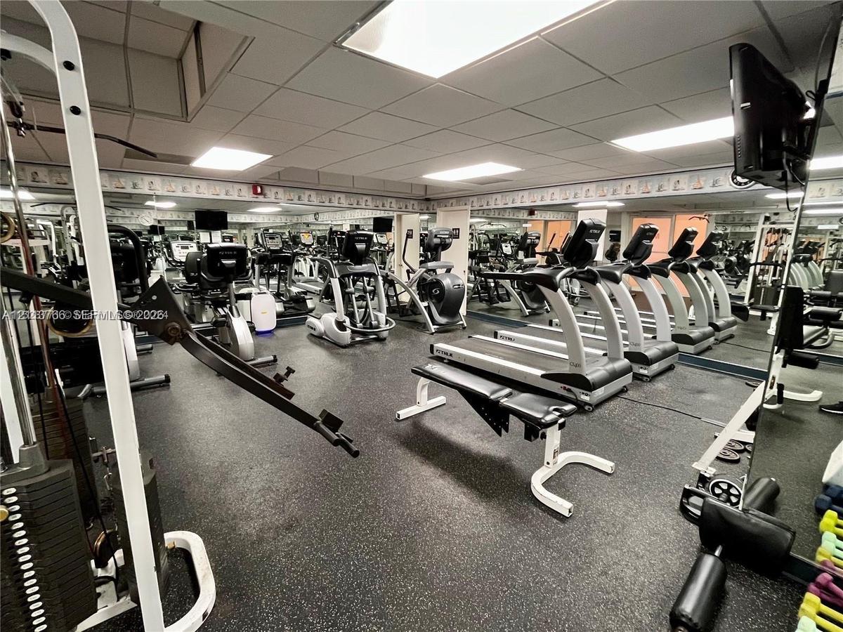Fitness center featuring wall-to-wall mirrors, recessed drop-ceiling lighting, and specialized rubberized flooring