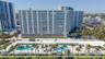 High-rise residential exterior featuring a multi-story facade, dual ground-level swimming pools, paved pool deck, and mature palm tree landscaping