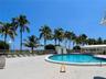 Circular swimming pool featuring a concrete deck, perimeter metal fencing, palm trees, and a covered pavilion