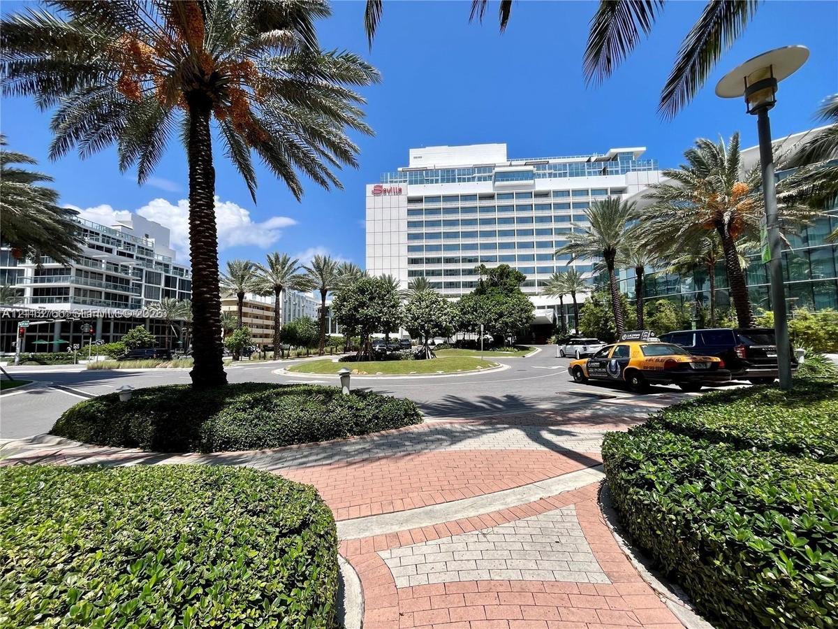 Exterior landscape featuring mature palm trees, manicured hedges, and decorative paver walkways
