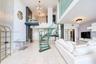 Double-height ceiling, glass-tread spiral staircase with metal railing, floor-to-ceiling textured accent wall, polished tile flooring, and glass mezza