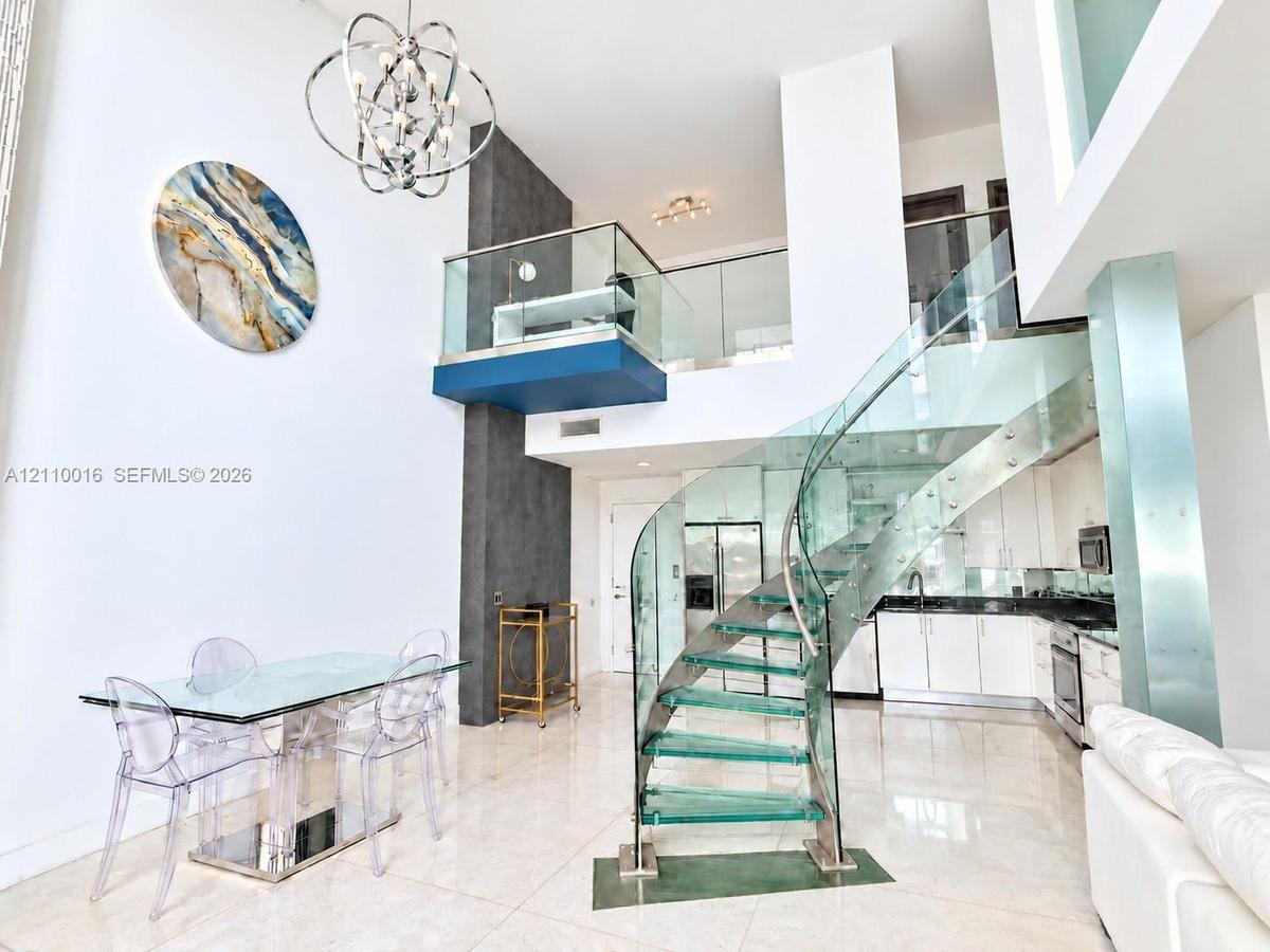 Curved staircase featuring glass treads and stainless steel railings, two-story ceiling, polished stone flooring, custom metal chandelier, and a glass