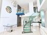 Curved staircase featuring glass treads and stainless steel railings, two-story ceiling, polished stone flooring, custom metal chandelier, and a glass