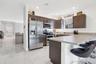 Kitchen featuring dark-finish cabinetry, stainless steel appliances, a peninsula with a stone-finish countertop, and light-toned tile flooring