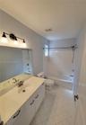 Bathroom featuring a white vanity with a solid surface countertop, an oval undermount sink, a three-light fixture, and a tub-shower combination with c