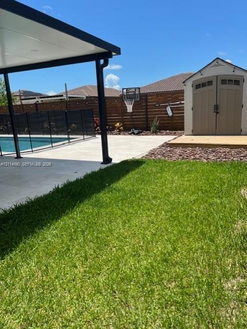 Backyard featuring a covered concrete patio, swimming pool with perimeter fencing, detached storage shed, and horizontal wood-slat privacy fencing