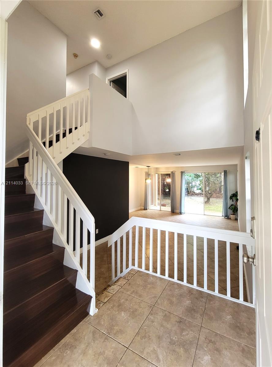 Foyer featuring high ceilings, wood-finish staircase treads, white balustrades, large-format tile flooring, and sliding glass doors