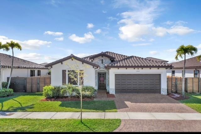 Single-story exterior featuring a tile roof, light-toned stucco finish, decorative stone accents, a brick-paver driveway, and a two-car garage
