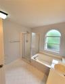 Bathroom featuring a soaking tub, separate glass-enclosed shower, arched window, and tile flooring