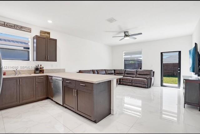 Kitchen featuring dark-finish cabinetry, neutral-toned countertops, stainless steel dishwasher, polished tile flooring, and a ceiling fan