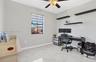 Room featuring large-format tile flooring, a central ceiling fan with an integrated light fixture, three mounted floating shelves, and a window equipp