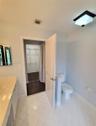Bathroom featuring a vanity with integrated sink and countertop, white tile flooring, enclosed water closet with half-wall, and walk-in closet with wi