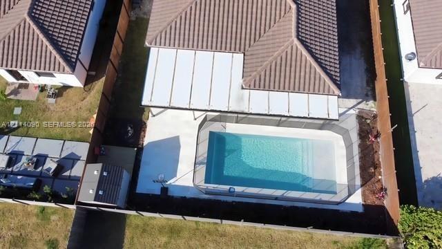 Aerial perspective of a backyard featuring a swimming pool with a surrounding mesh safety fence, a concrete patio, a covered pergola, and a storage sh