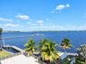 Waterfront terrace featuring stone paving, metal railings, mature palm trees, a dedicated boat dock, and direct access to open water