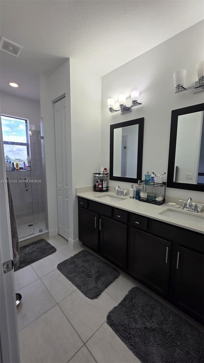 Dual vanity with dark cabinetry, light-toned countertop, framed mirrors, and glass-enclosed shower with tile flooring