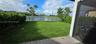 Backyard featuring a paved patio, manicured lawn, perimeter hedge fencing, and metal enclosure overlooking a pond