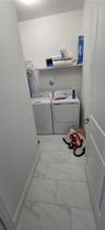 Dedicated laundry alcove featuring large-format stone-patterned tile flooring and an integrated wall-mounted shelf