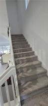 Staircase featuring wall-to-wall carpeting, white railing with vertical balusters, and high-reaching walls