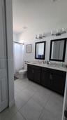 Double vanity with dark cabinetry, stone-finish countertops, dual framed mirrors, and large-format neutral tile flooring